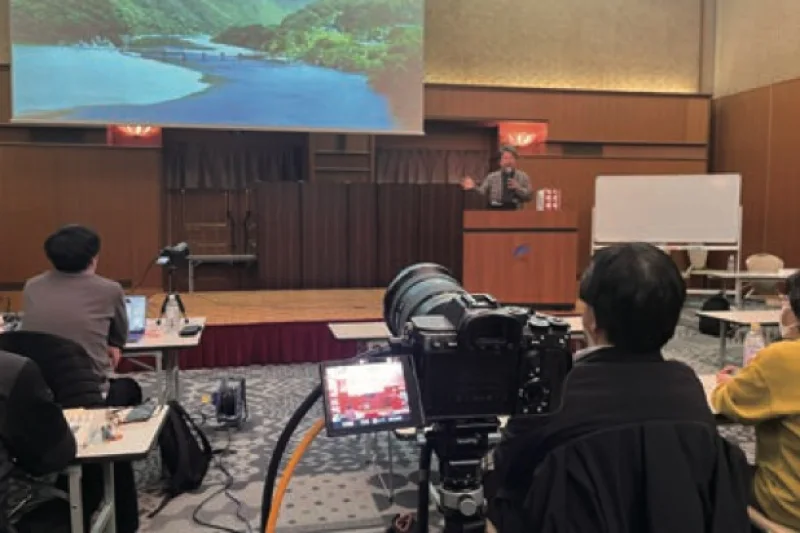 ホテルの会場から配信するセミナーの現場。カメラ越しに演台とスクリーン
