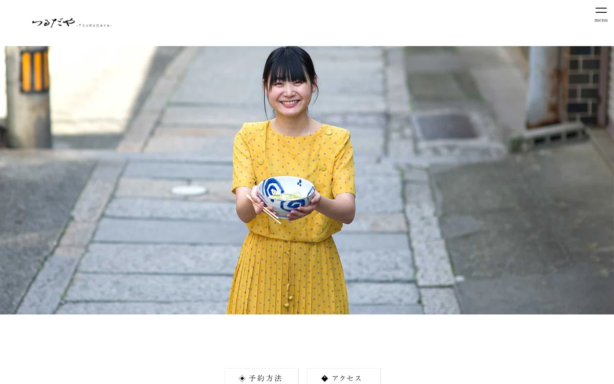 つるだやのWebサイト。参道でうどんの丼を持つ人物の写真がトップに置かれている