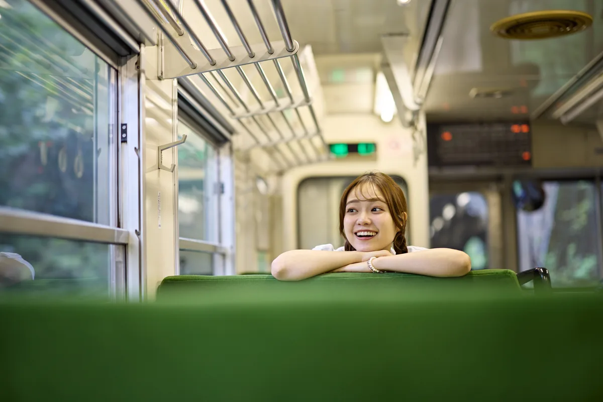 電車の座席の背にひじをついて笑う女性