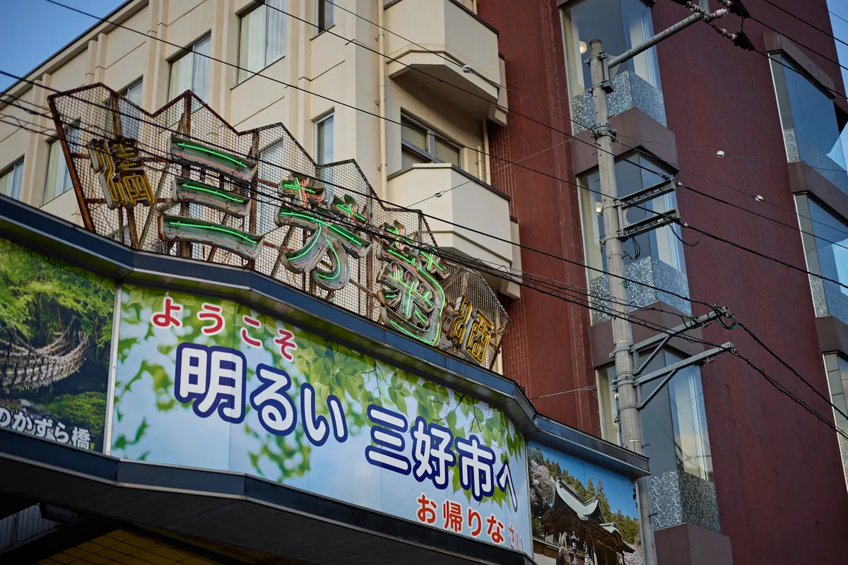 「ようこそ 明るい三好市へ」と書かれた駅前の看板と、ネオン看板