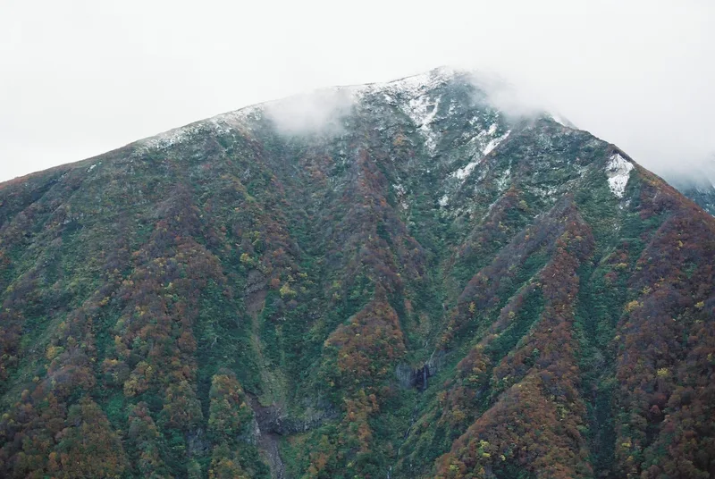 紅葉の山肌と、雪をかぶった山頂