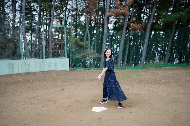 松林に囲まれたグラウンドで、ホームベースを踏んで走る女性