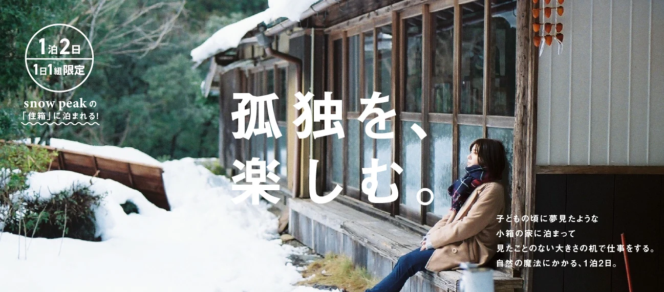 告知バナー「孤独を、楽しむ。」雪の残る古い建物の縁側に座る女性